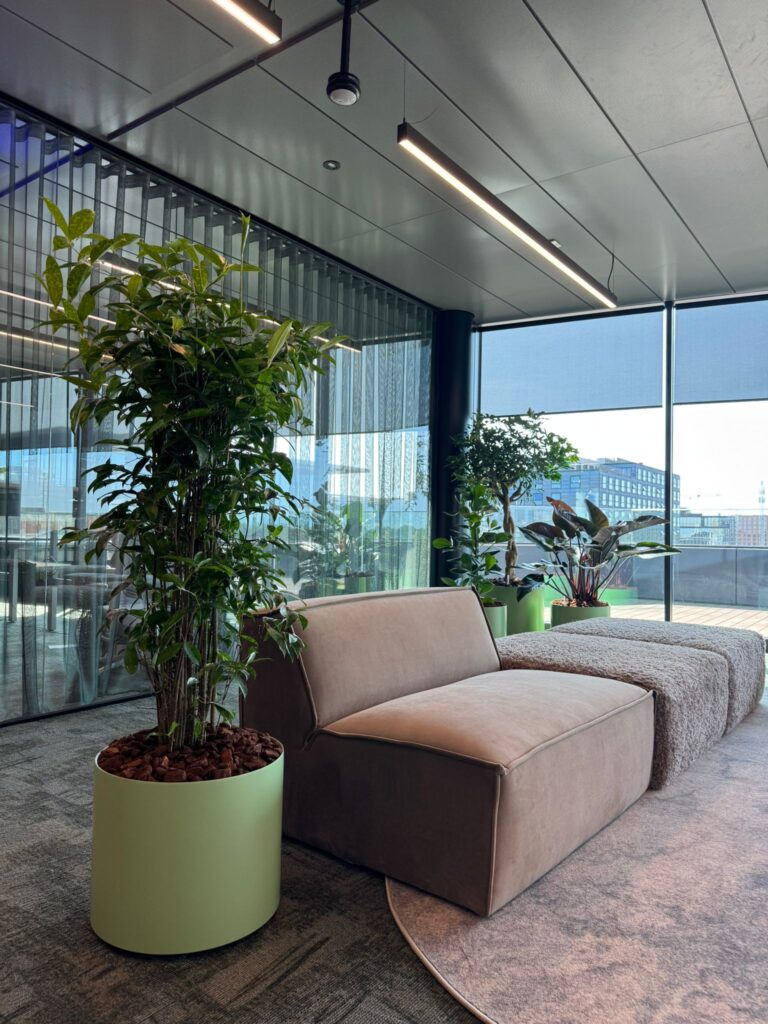 Moderne werkruimte met grote kamerplanten en uitzicht over het water, ingericht door Bloei.
